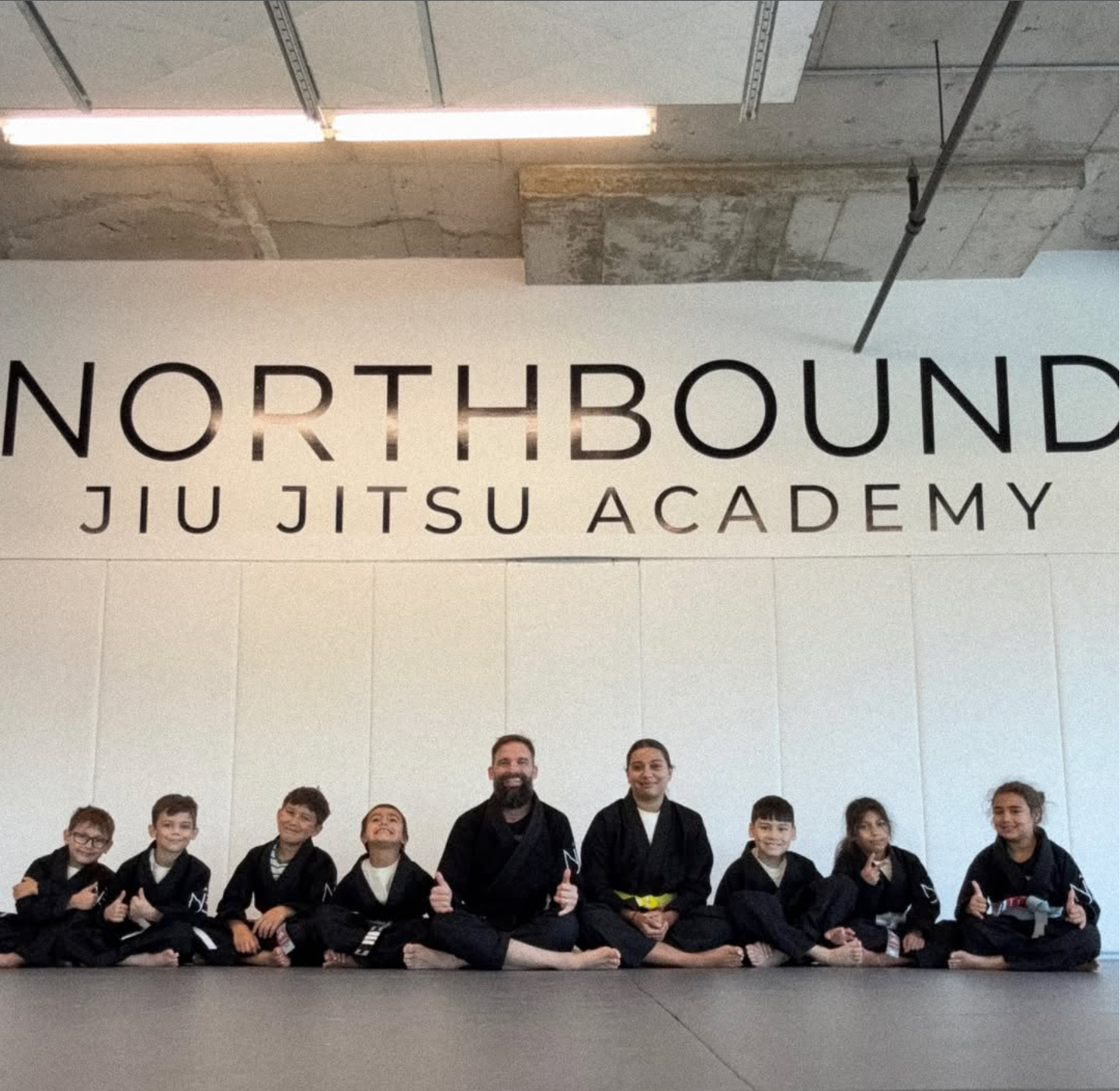 Enfants et entraîneurs assis ensemble sous l’enseigne Northbound Jiu Jitsu Academy