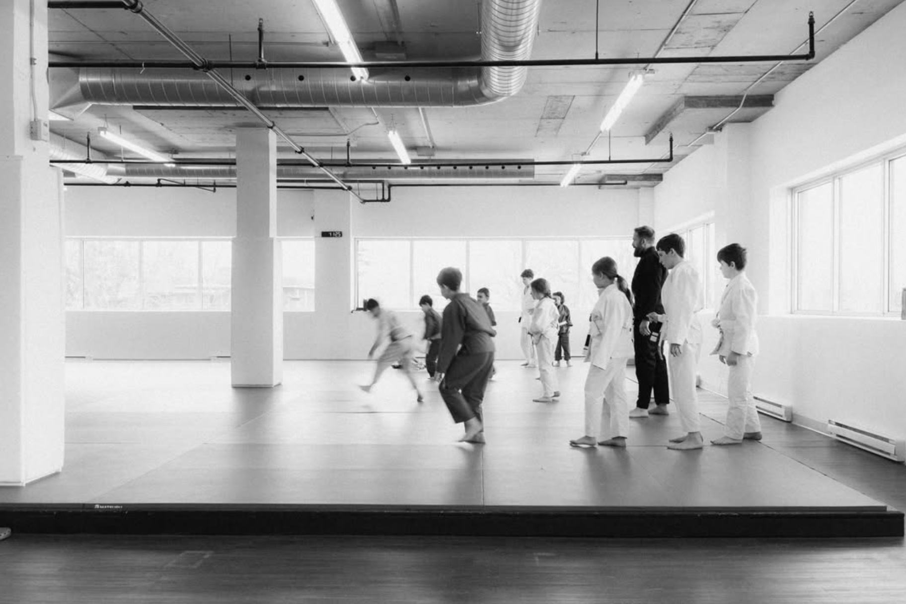 Enfants qui pratiquent des déplacements sur les tatamis avec un entraîneur pendant un cours de jiu-jitsu chez Northbound