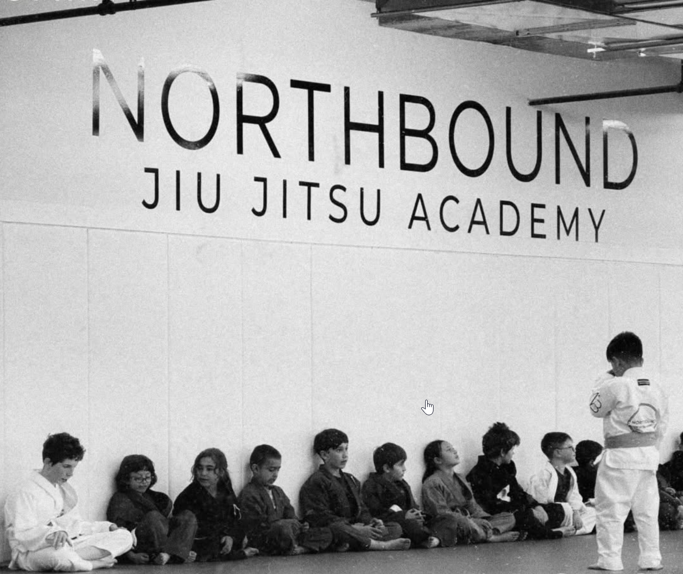 Enfants assis ensemble le long des tatamis sous l’enseigne Northbound Jiu Jitsu Academy pendant un cours